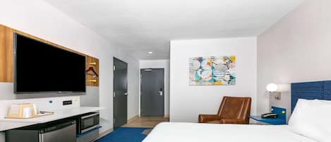 A hotel room with a bed, a desk with a flat-screen TV, a microwave, and a seating area with a chair.