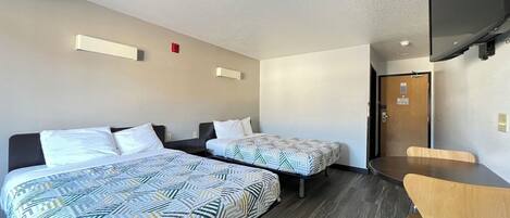 A hotel room with two beds, a desk, and a chair. There is a television mounted on the wall and a door leading to another room.