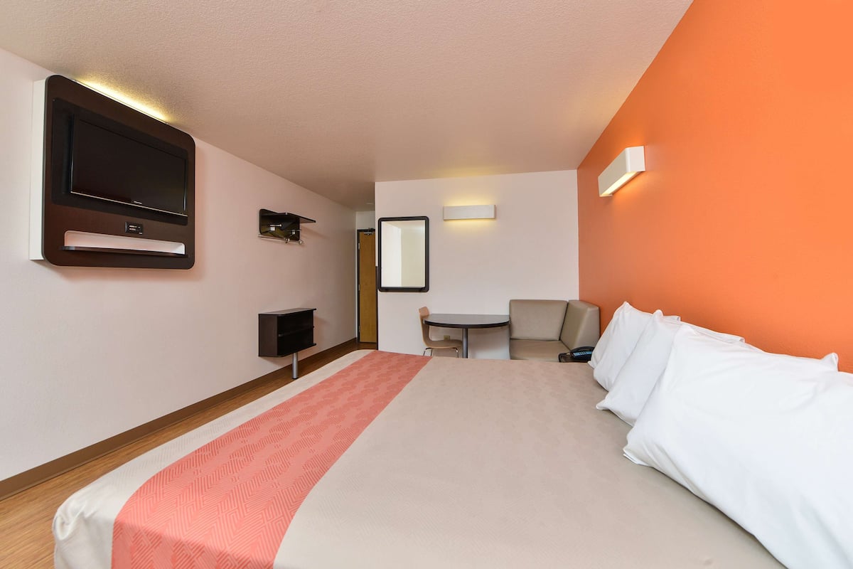 Ein Hotelzimmer mit Bett, Schreibtisch, Stuhl, Fernseher und Spiegel.