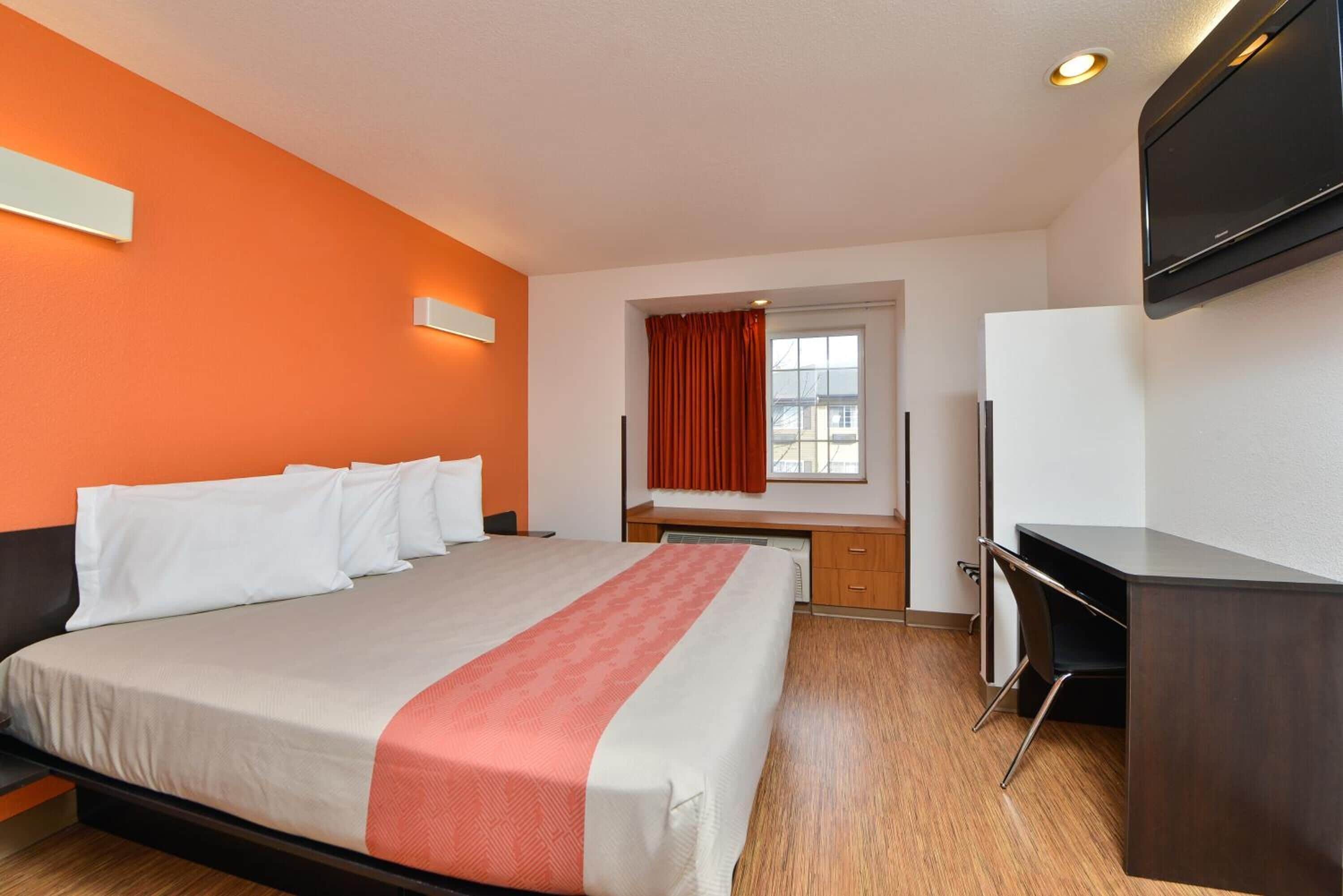 A hotel room with a bed, a desk, a chair, a television, and a window with curtains.