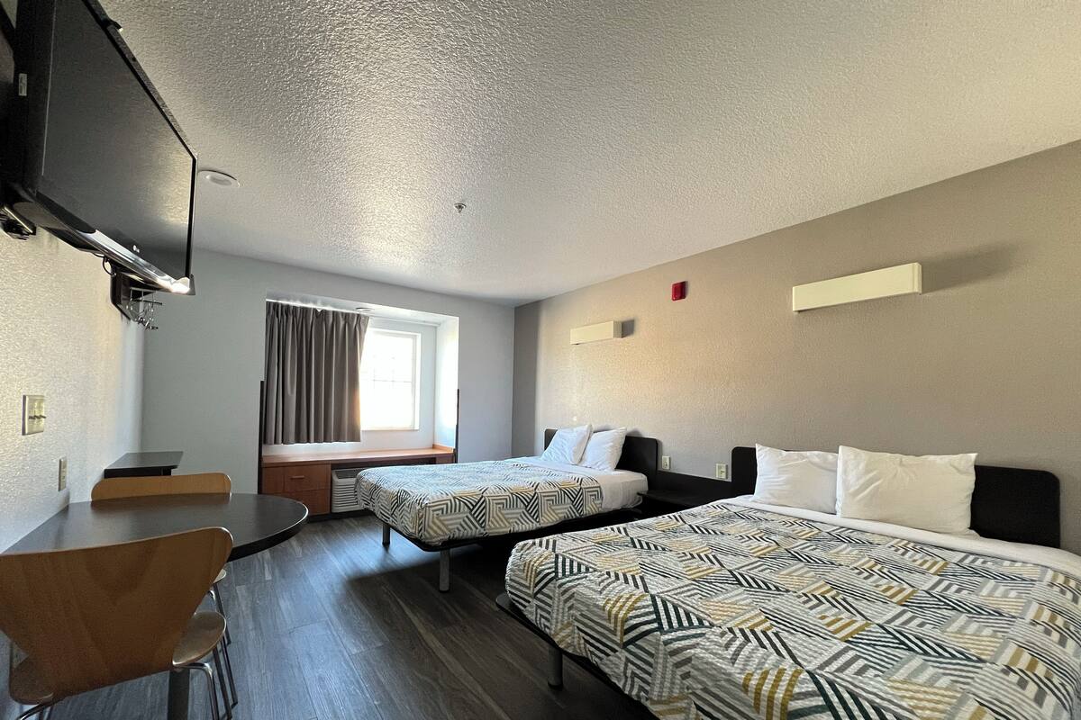 Ein Hotelzimmer mit zwei Betten, einem Schreibtisch, einem Stuhl, einem Fernseher und einem Fenster mit Vorhängen.
