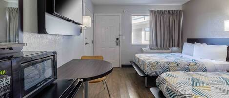Quarto de hotel com cama, escrivaninha com micro-ondas, cadeira e janela com cortinas.