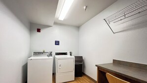 A laundry room with two washers and a dryer, a small trash bin, and a wooden desk.