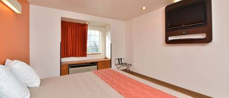A hotel room with a bed, a TV mounted on the wall, a window with curtains, and a radiator.