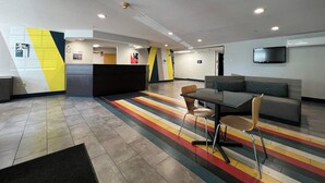 A modern lobby with a reception desk, seating area, and a flat-screen TV mounted on the wall.