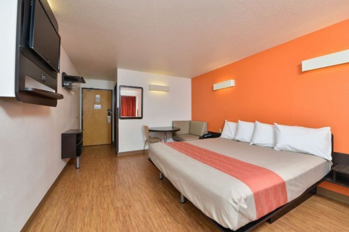 A hotel room with a bed, a desk, a chair, a TV, and a door.