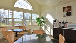 A conference room with a glass table, wooden chairs, a potted plant, and a coffee station with branded coffee makers.