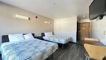 Una habitación de hotel con dos camas, una mesa de madera y un televisor en la pared.
