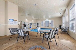 Zona junto a la piscina con sillas y mesas, piscina y techo con ventilación.
