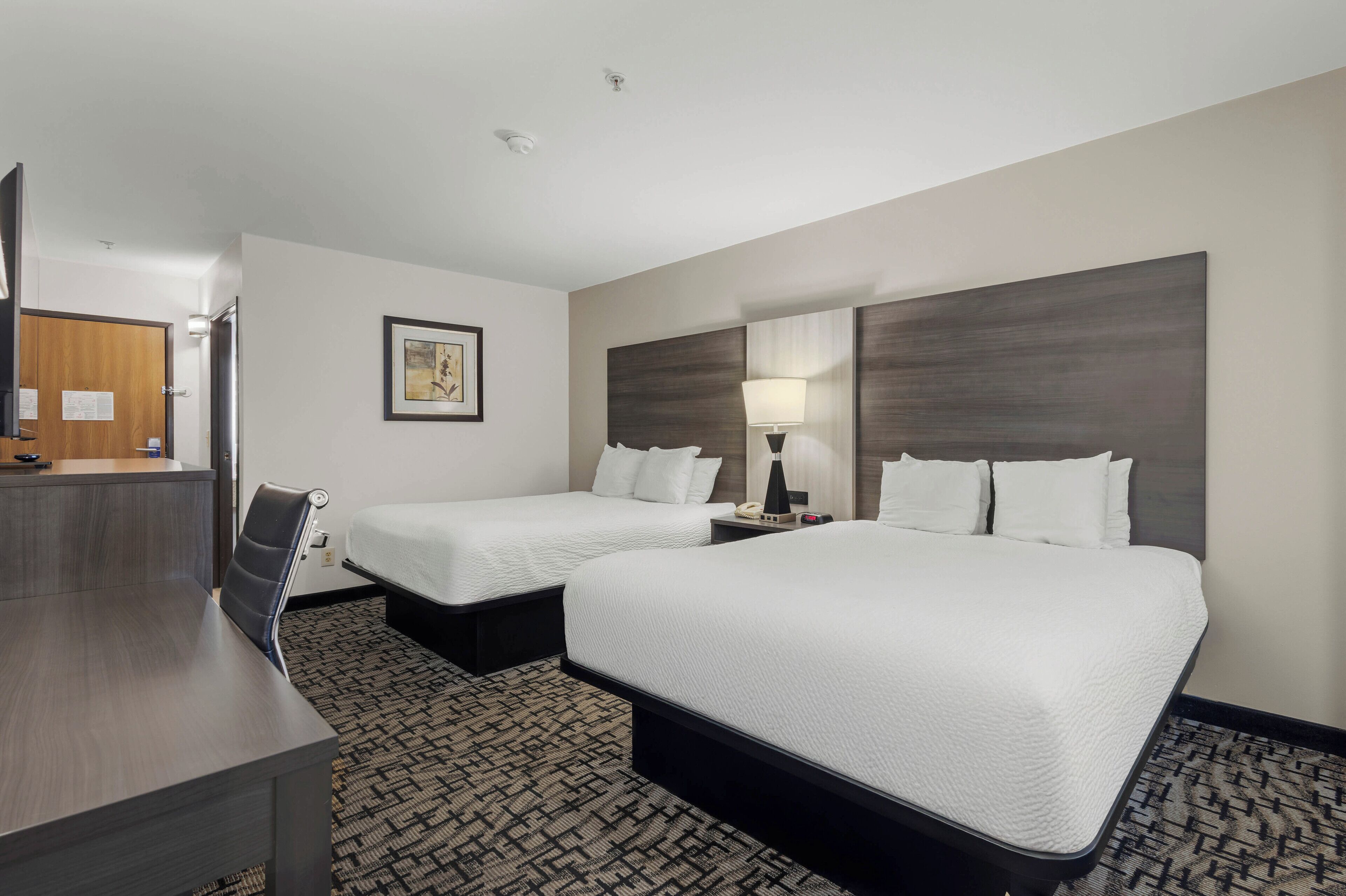 A hotel room with two beds, a desk, and a chair.