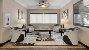 A modern room with a central table, two chairs, a ceiling fan, and a large window with blinds. - Best Western Crown Inn & Suites (Batavia)