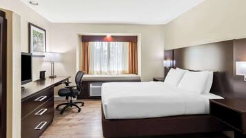 A hotel room with a bed, desk, chair, and a window with curtains.