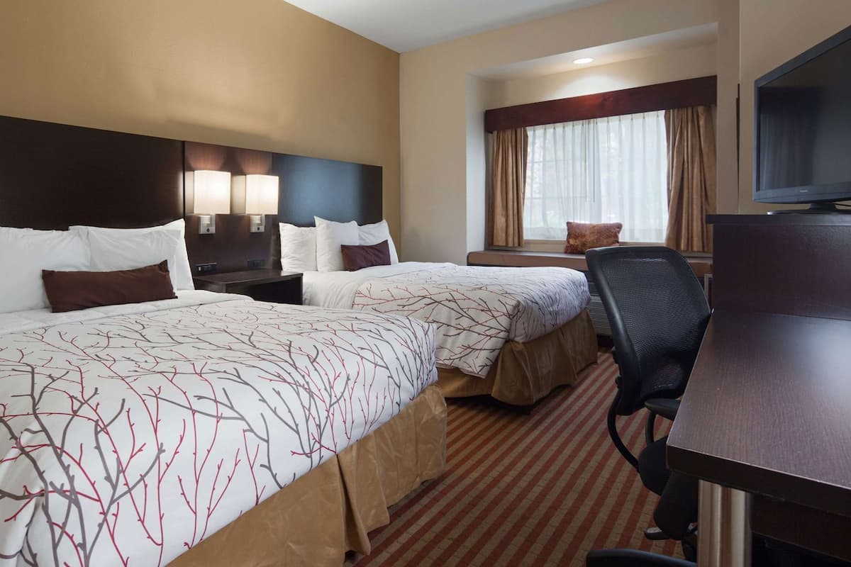 Quarto de hotel com duas camas, uma escrivaninha, uma cadeira, uma televisão e uma janela com cortinas.