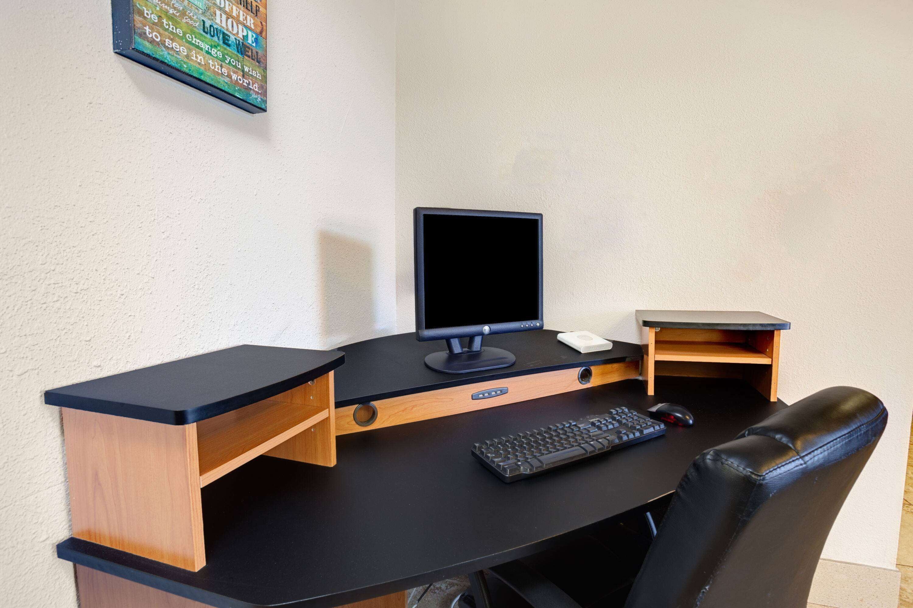 Un espacio de trabajo reducido con una computadora, teclado, ratón y una pequeña estantería.