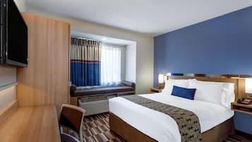 A hotel room with a bed, a desk, a chair, a TV, a window with curtains, and a nightstand with a lamp.