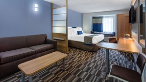 Una habitación de hotel compacta con cama, sofá, escritorio y televisor.