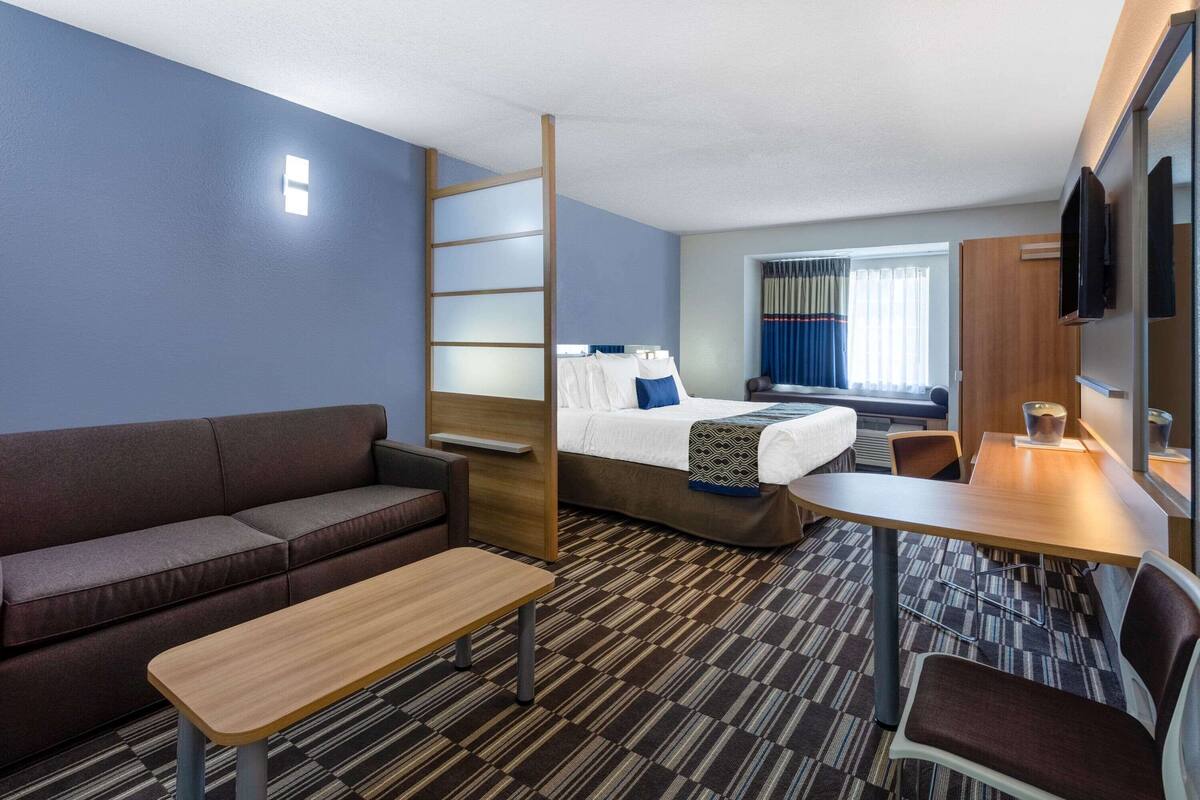 A compact hotel room with a bed, a sofa, a desk, and a TV.