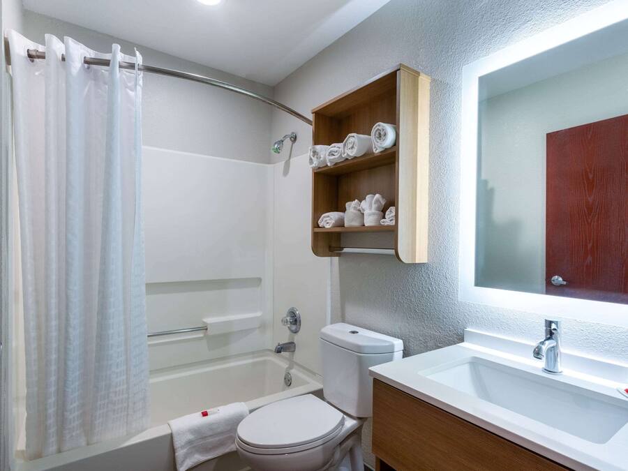 A bathroom with a shower, toilet, and sink. There are shelves with towels and a mirror above the sink.
