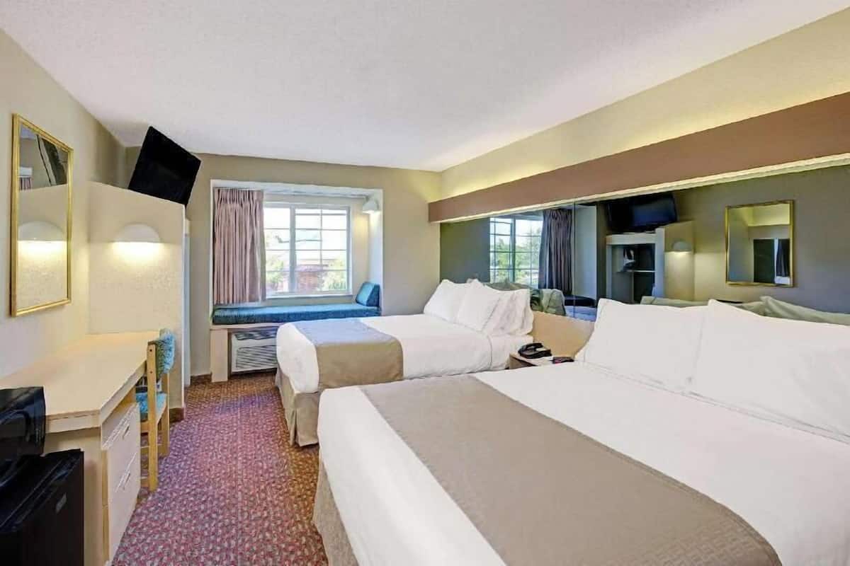 A hotel room with two beds, a desk, a television, and a window with curtains.