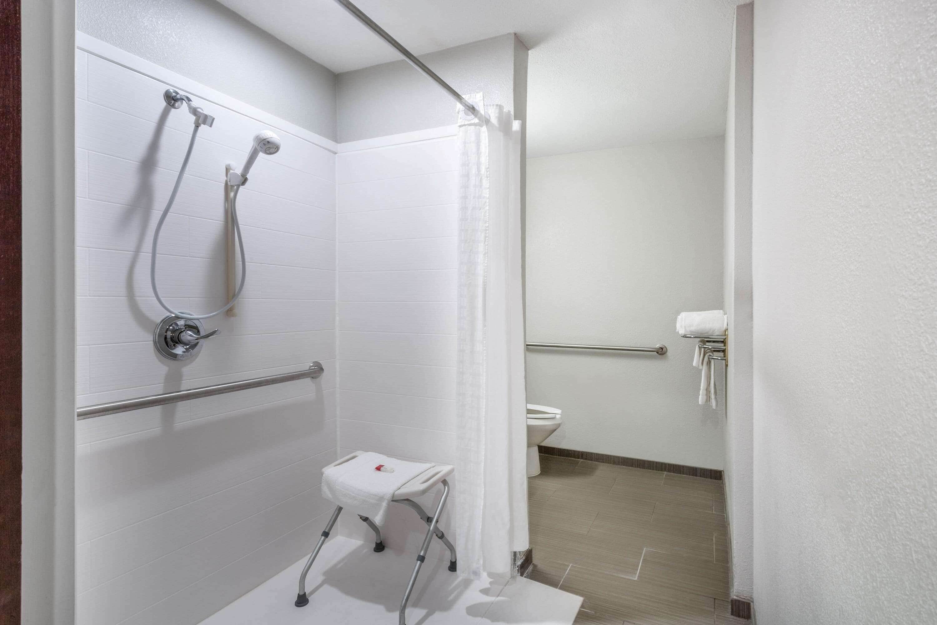 A bathroom with a shower, toilet, and a small white stool.