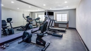 Un gimnasio con máquinas de cardio, un espejo y una televisión en la pared.