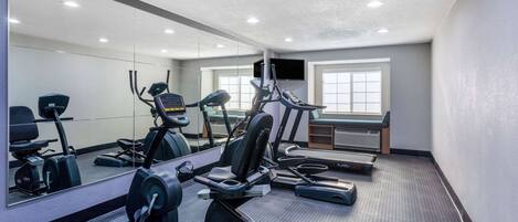 Un gimnasio con máquinas de cardio, un espejo y una televisión en la pared.