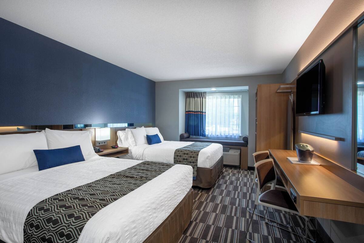 A hotel room with two beds, a desk, a TV, and a window with curtains.