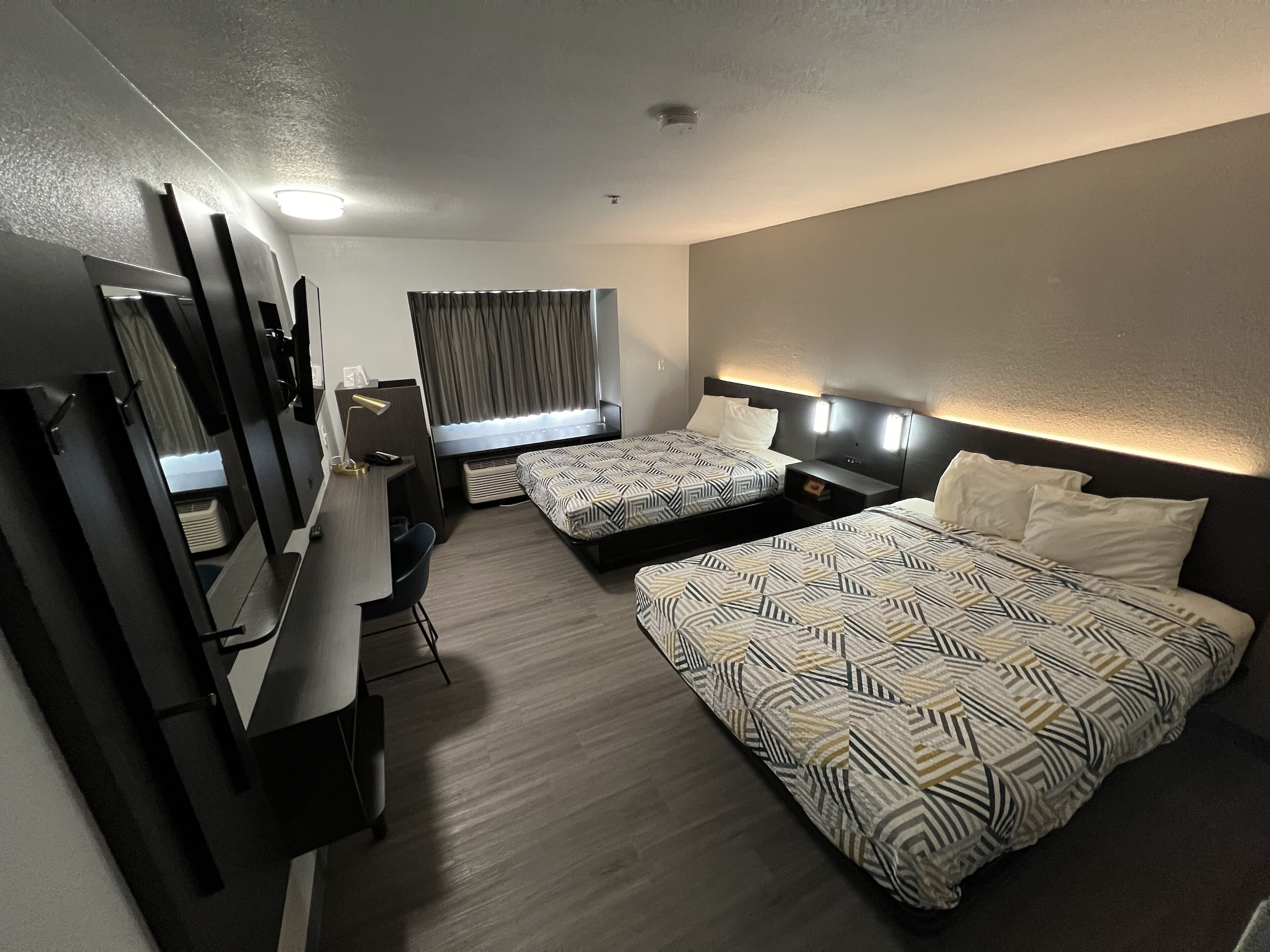 Habitación de hotel con dos camas, un escritorio, una silla y un televisor.