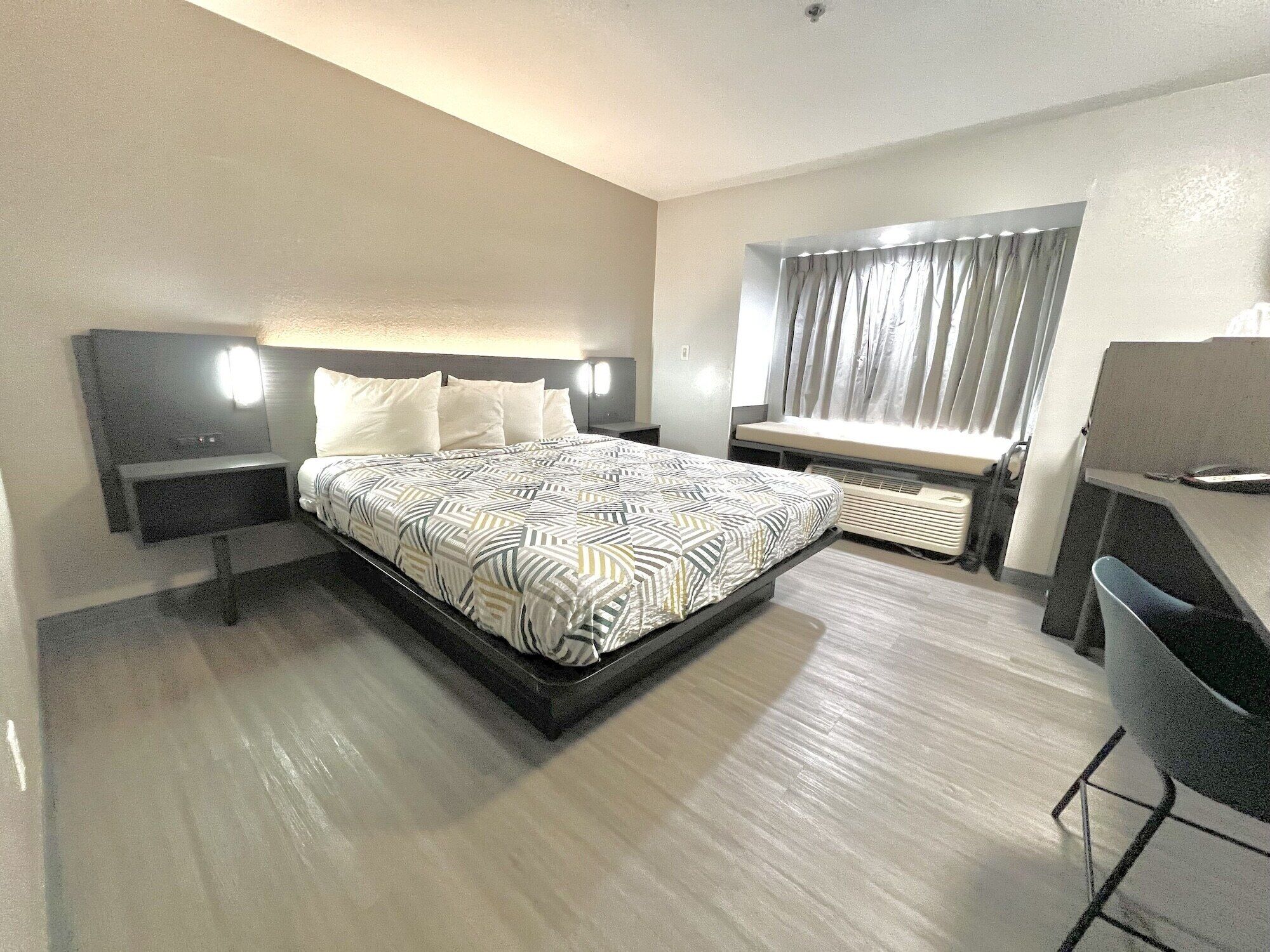 Ein Hotelzimmer mit einem großen Bett, Nachttischen, einem Schreibtisch und einem Fenster mit Vorhängen.