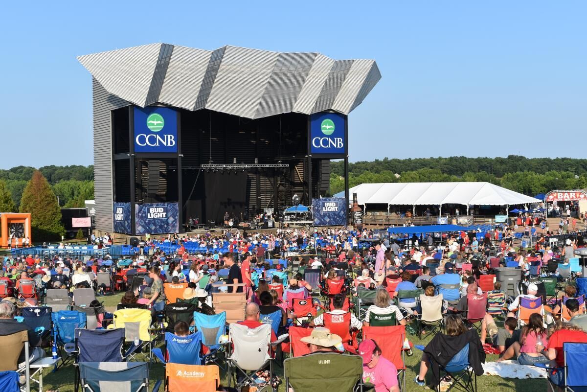 A large outdoor event with a stage and audience seated in various chairs.