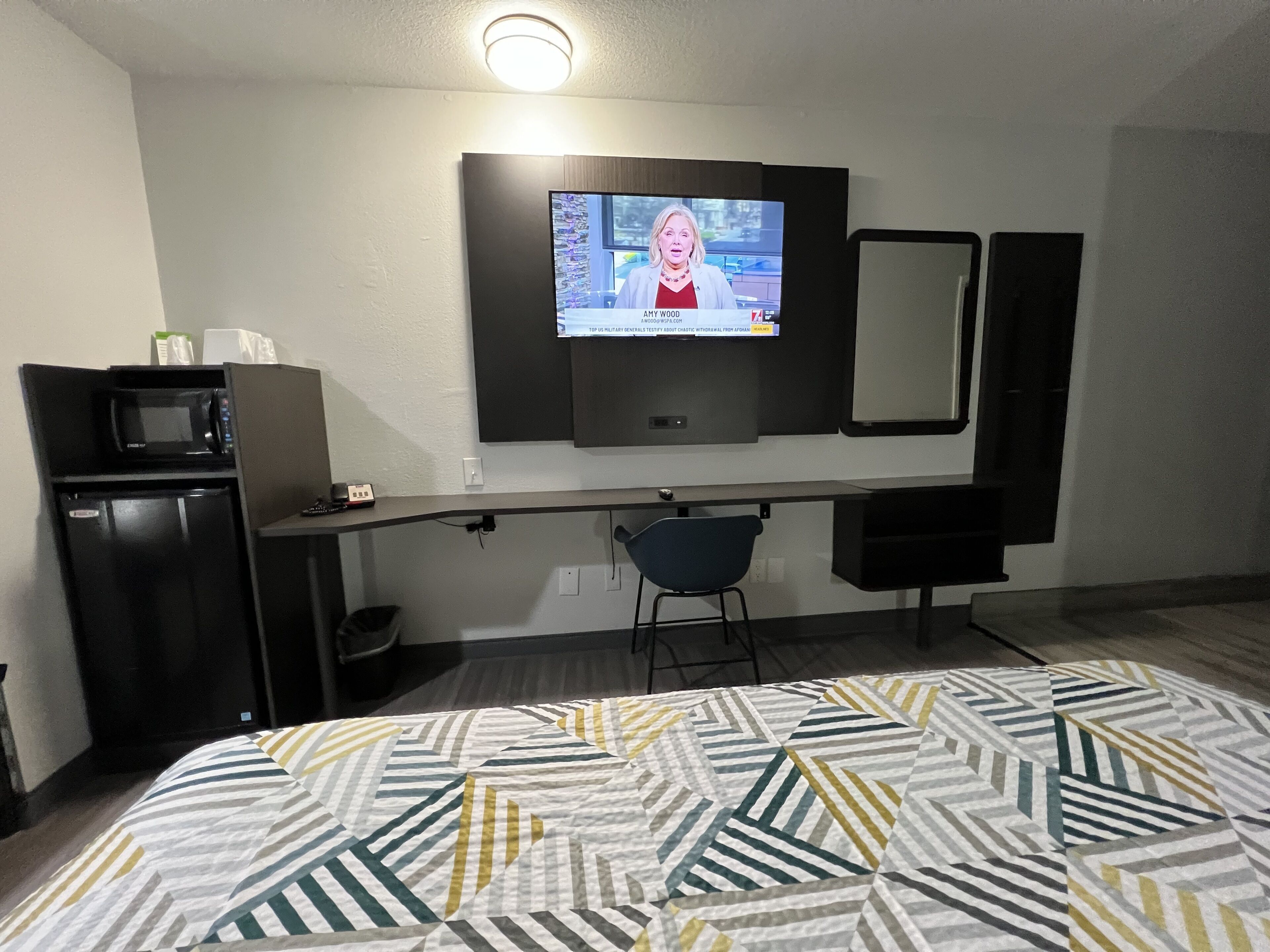 Una habitación de hotel con cama, escritorio con silla, televisor, microondas y refrigerador.