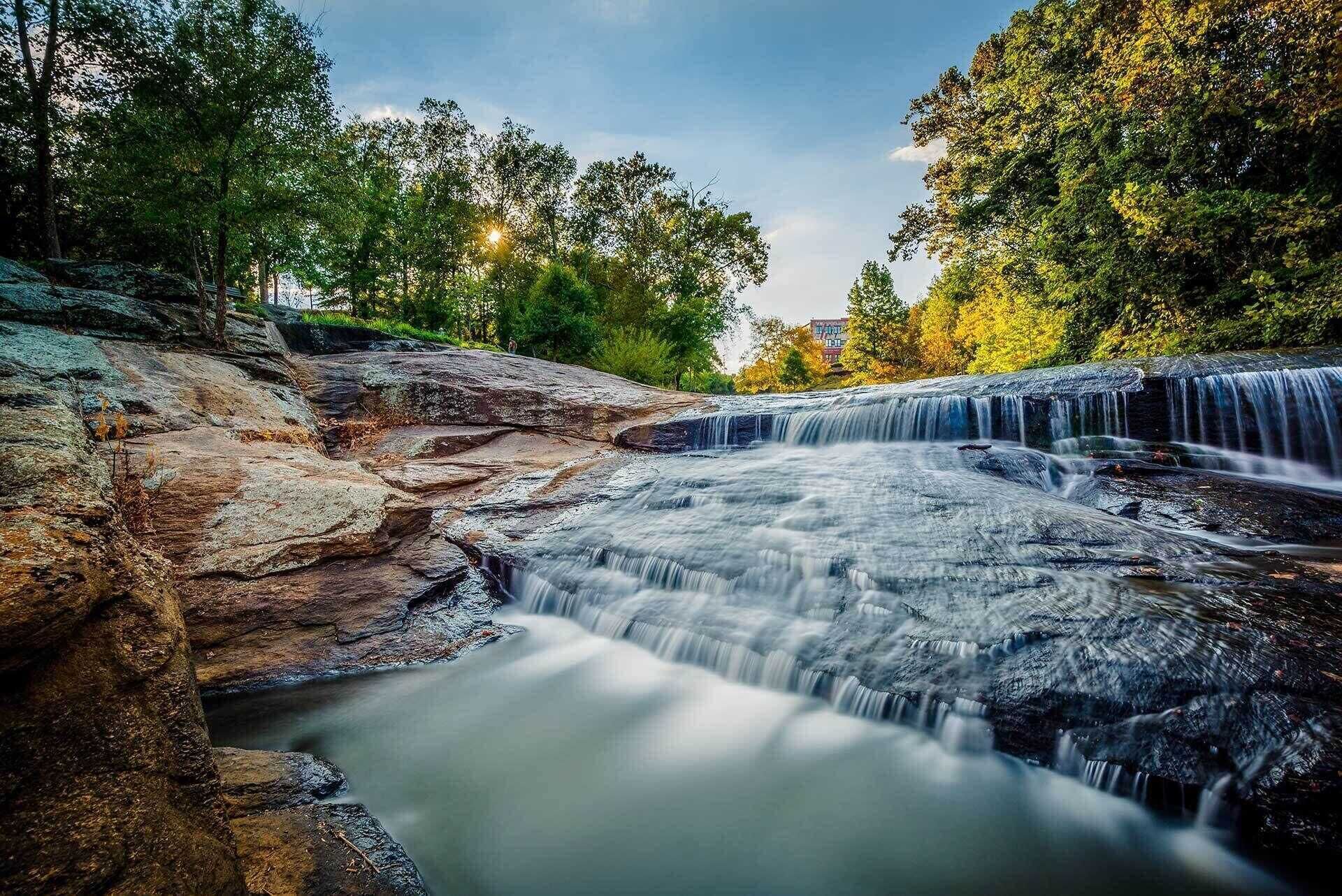 Una cascada que se precipita sobre rocas con un paisaje boscoso de fondo.