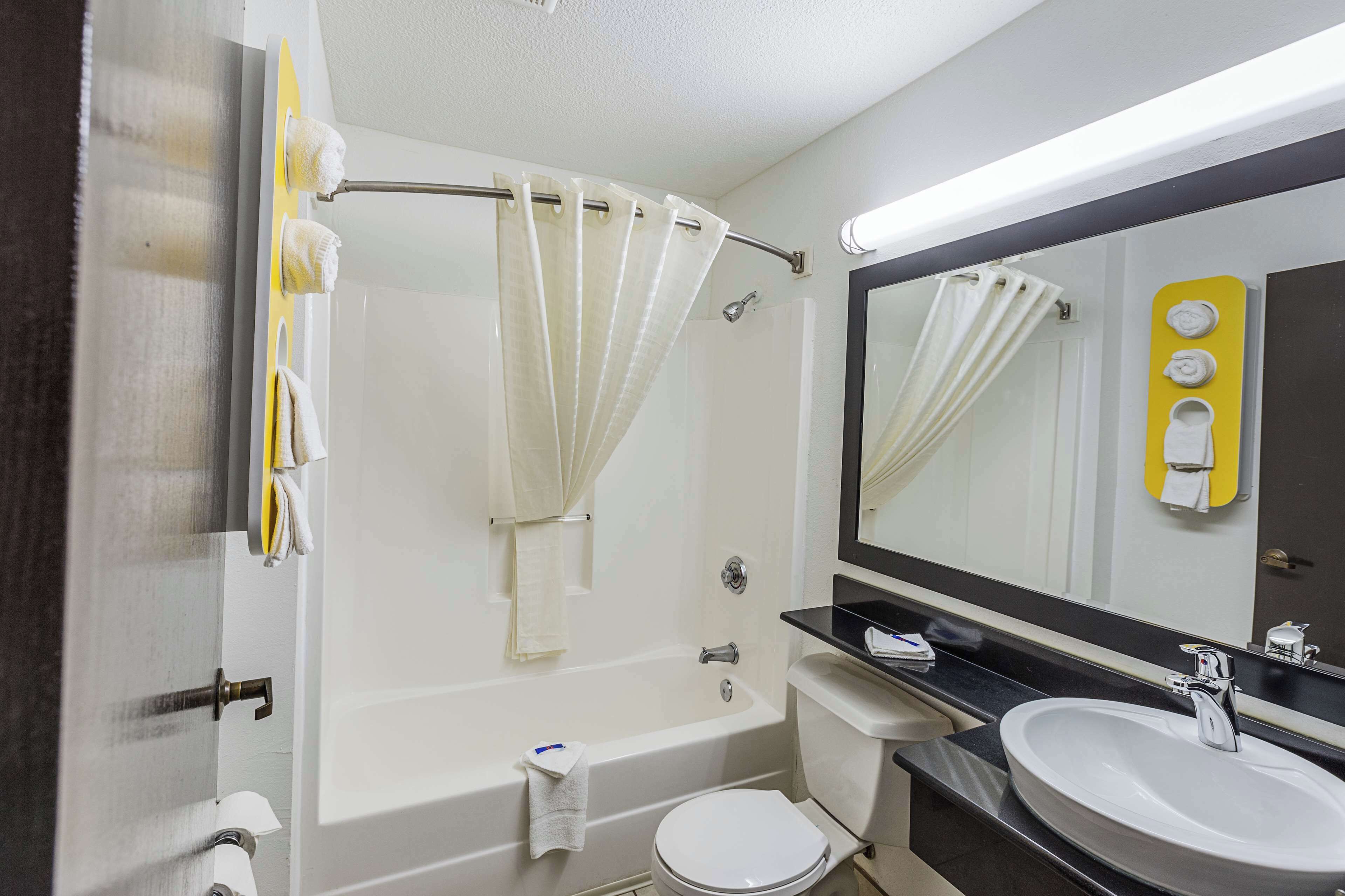 Un baño con bañera, inodoro, lavamanos y un espejo grande.