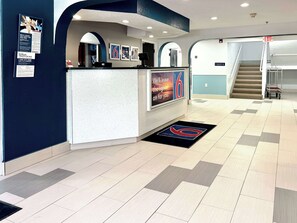 Welcome to our hotel, where a modern reception area awaits with a digital screen, framed artwork, and a stylish staircase.