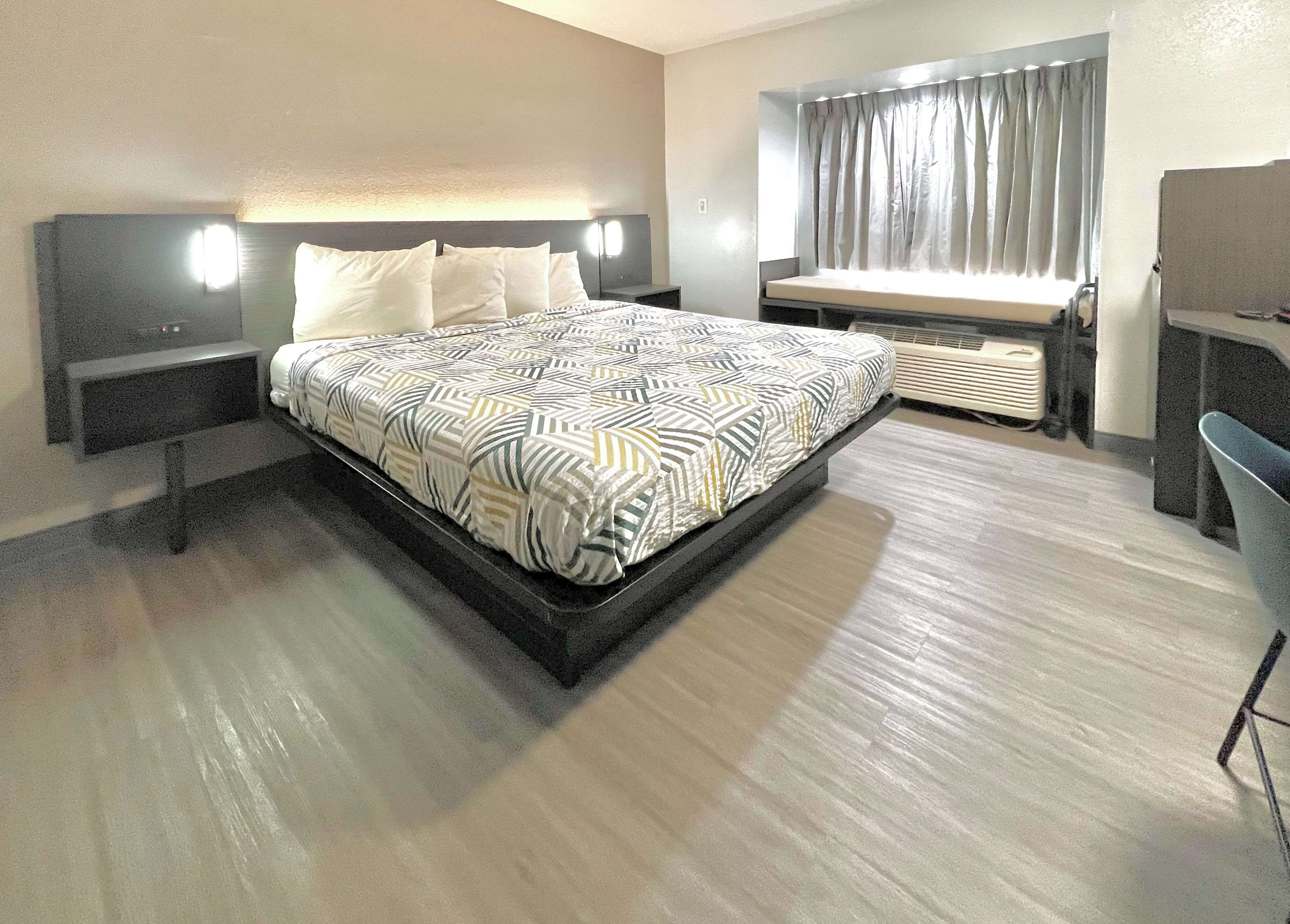 A modern hotel room with a large bed, bedside tables, a desk, and a window with curtains.