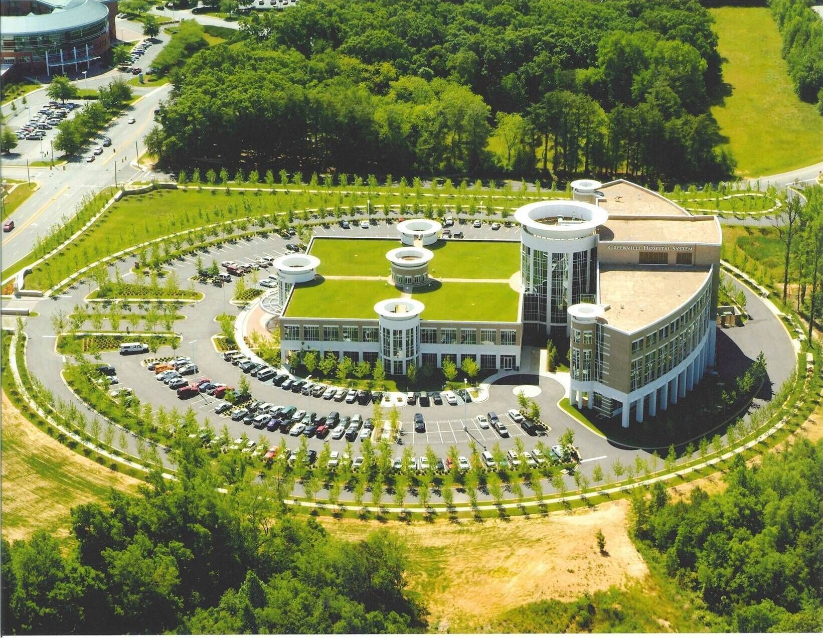 A hospital complex with a central circular building, a parking area, and surrounding greenery.