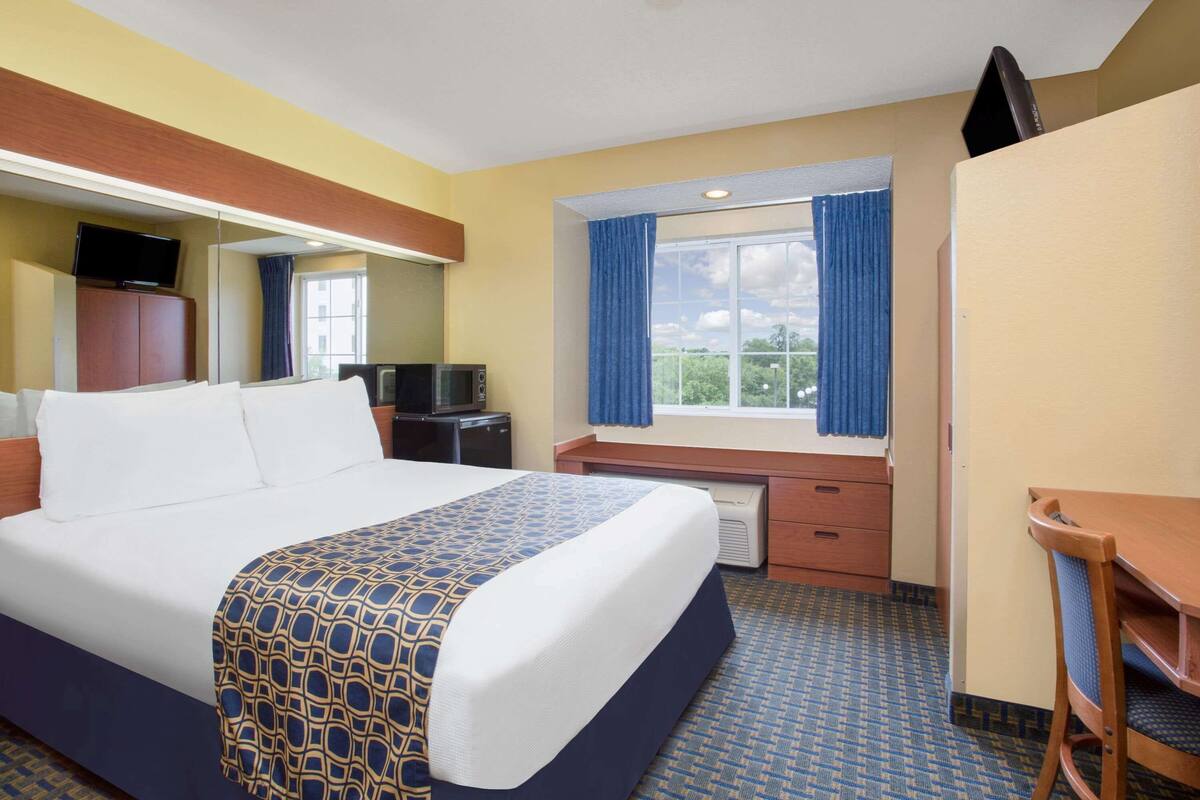 A hotel room with a large bed, a desk, a chair, a television, and a window with curtains.
