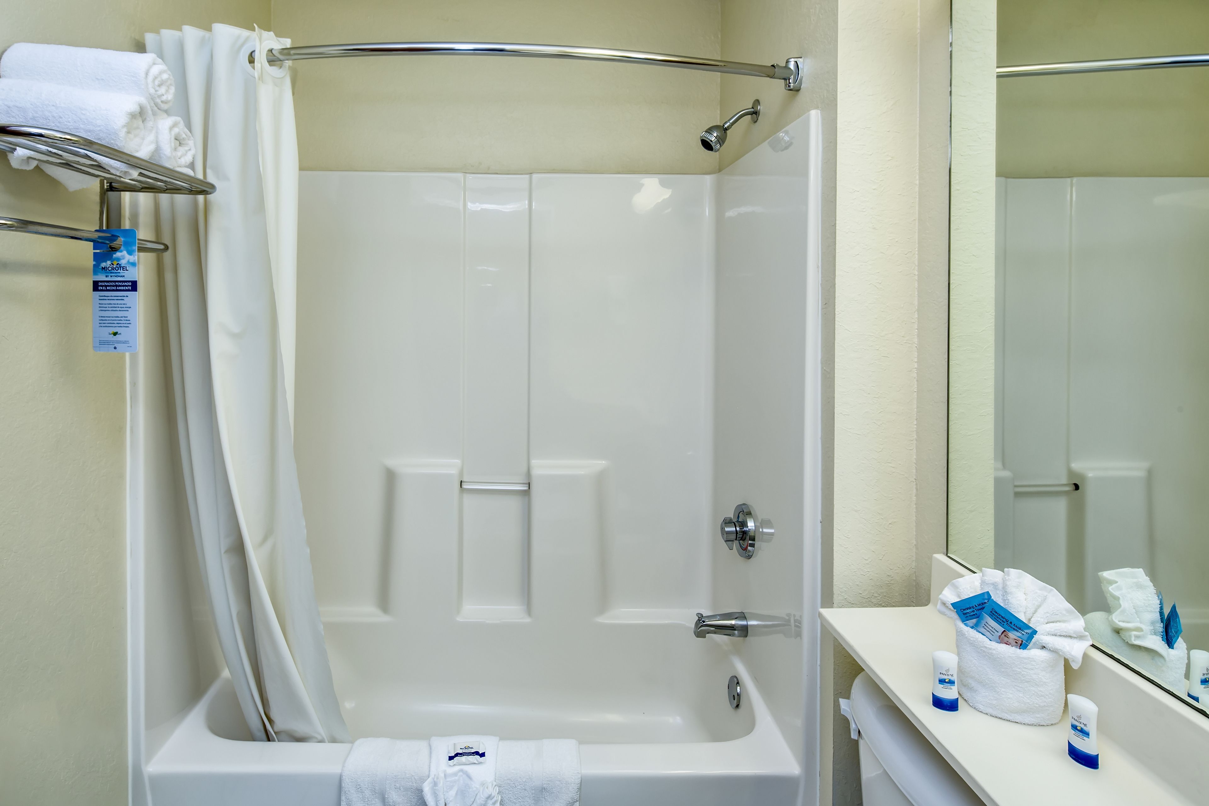 Baño de hotel con bañera, ducha y tocador con artículos de aseo.