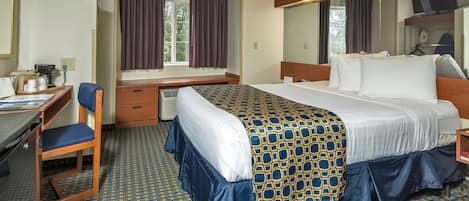 A hotel room with a bed, a desk, a chair, a window with curtains, and a television.