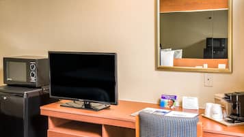 A hotel room with a desk, a television, a microwave, a coffee maker, and a mirror.