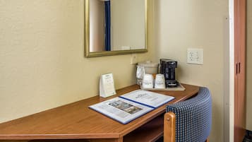 Een hotelkamer met een houten bureau, een spiegel, een koffiezetapparaat, een telefoon en een brochure op het bureau.