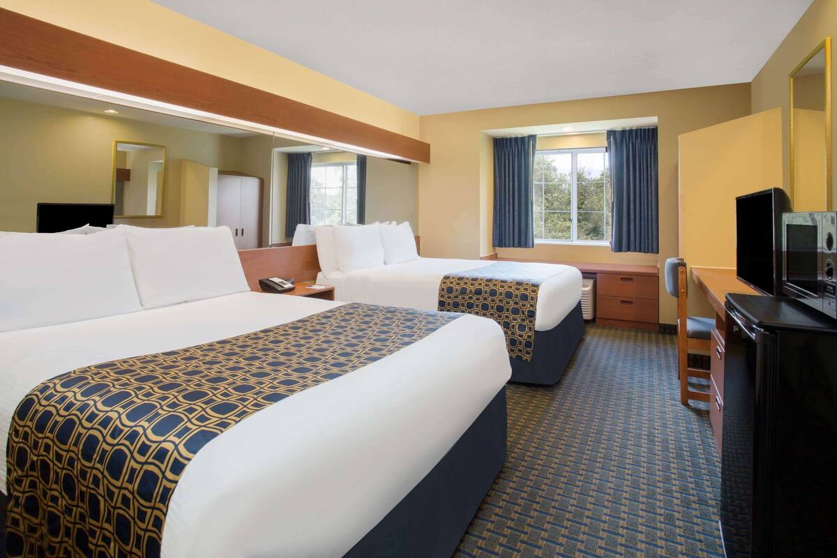 A hotel room with two beds, a desk, a TV, and a mirror.
