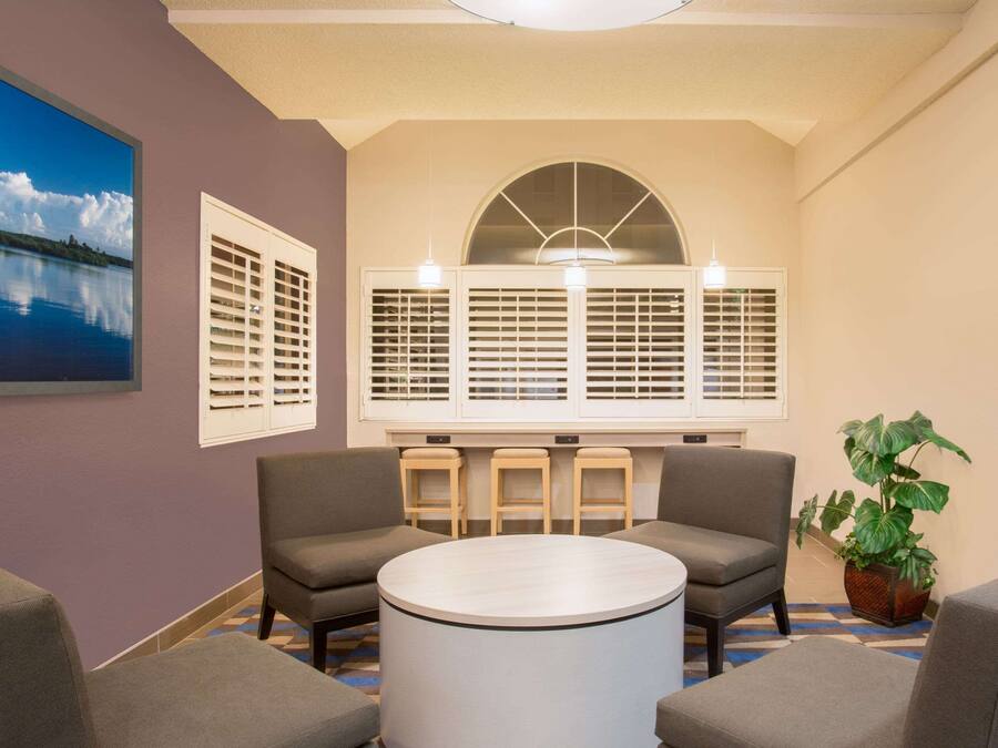 A room with a round table, two sofas, a large window with shutters, and a potted plant.