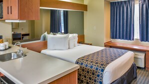 A hotel room with a bed, a small desk, a mirror, a window with curtains, a sink, and a microwave. - Microtel Inn & Suites by Wyndham Leesburg/Mt Dora (Leesburg)
