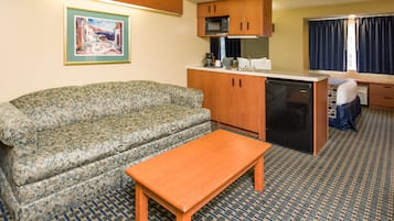 A compact living space with a sofa, a small wooden table, a kitchenette with a microwave, and a dishwasher.
