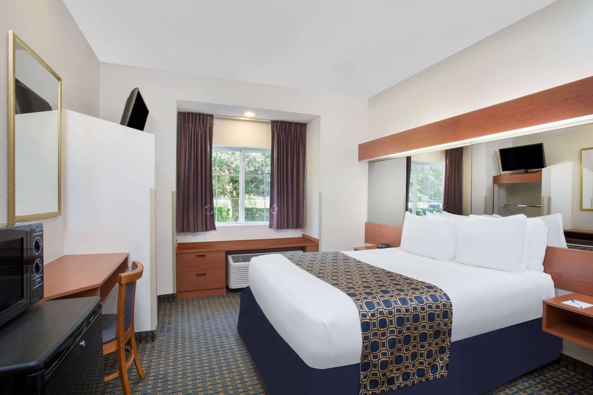 A hotel room with a bed, a desk, a chair, a television, and a window with curtains.