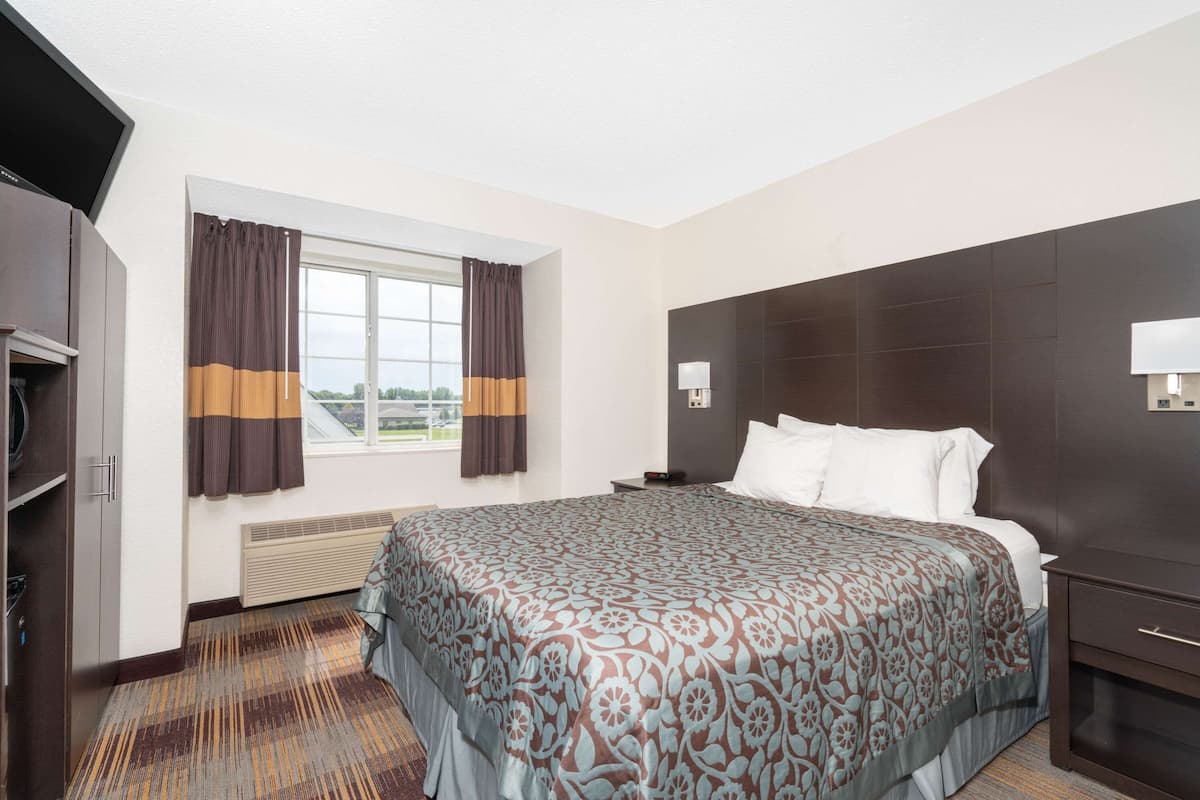 A hotel room with a large bed, a TV, a desk, and a window with curtains.