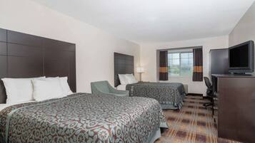 Ein Hotelzimmer mit zwei Betten, einem Schreibtisch, einem Fernseher und einem fensterbepflanzten Fenster.