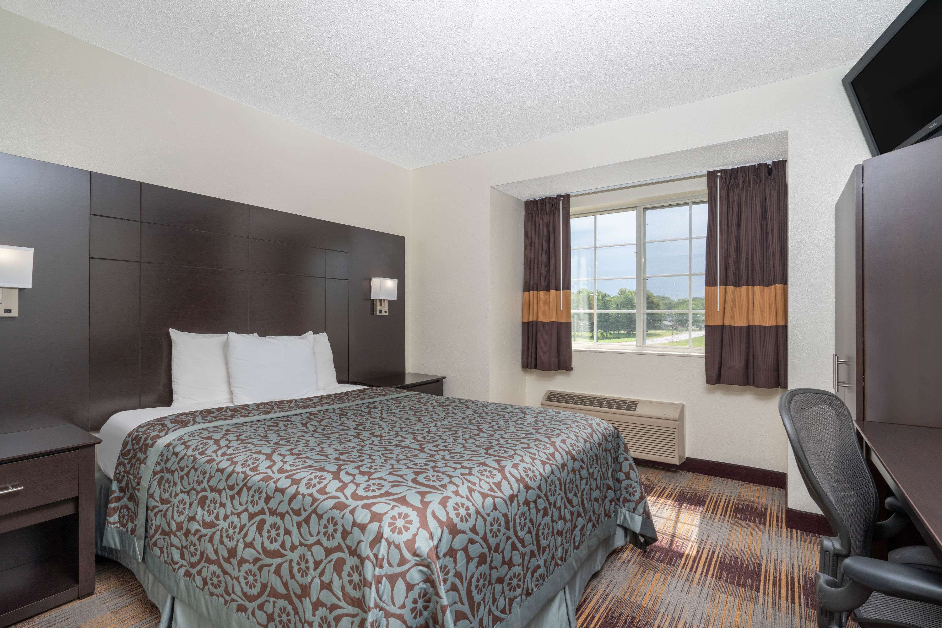 A hotel room with a large bed, a desk, a chair, a TV, and a window with curtains.