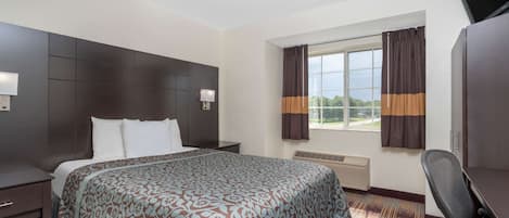 A hotel room with a large bed, a desk, a chair, a TV, and a window with curtains.